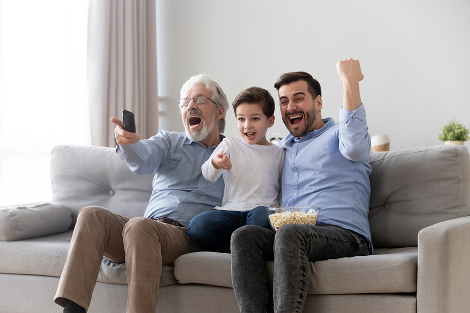 Photo of three males—child, middle aged, and elderly—cheering in reaction to TV