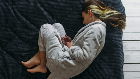 A woman lies curled up in fetal position on a bed