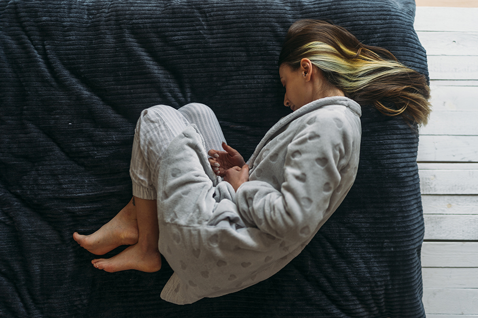 A woman lies curled up in fetal position on a bed
