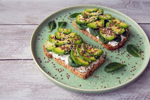 Toast with cream cheese and avocado displayed on a green plate with flax seeds spread across. 