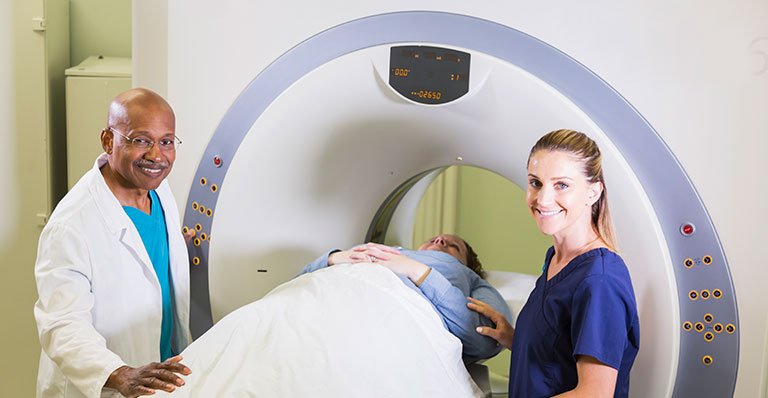 two smiling medical professionals comfort a patient lying in a CT scan machine