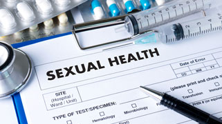 A paper form on a clipboard titled Sexual Health, surrounded by syringes, pills, a pen, and a stethoscope